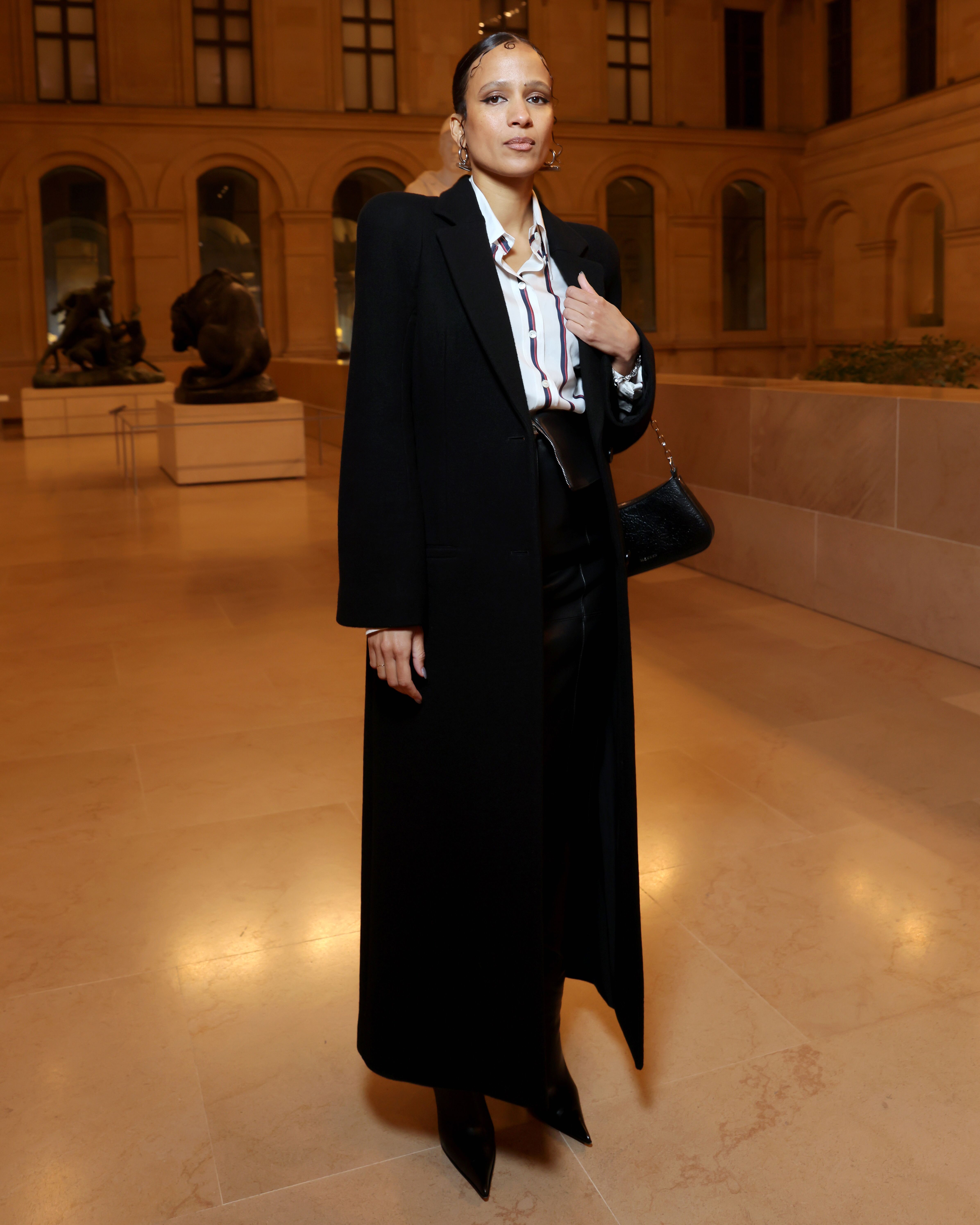 Mati Diop wears a striped silk shirt with open waistband pencil skirt and black washed wool moulded shoulder coat 