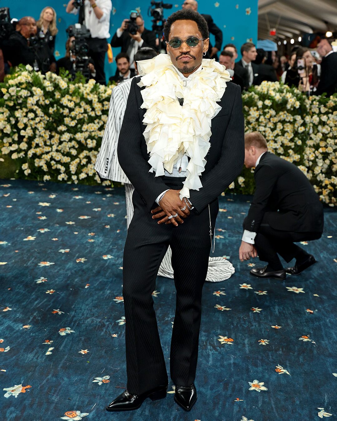 Kaytranada wearing McQueen ivory-toned ruffled collar shirt with Autumn Winter 2025 tailored jacket and metal t-bar oval sunglasses on Met Gala 2025 carpet