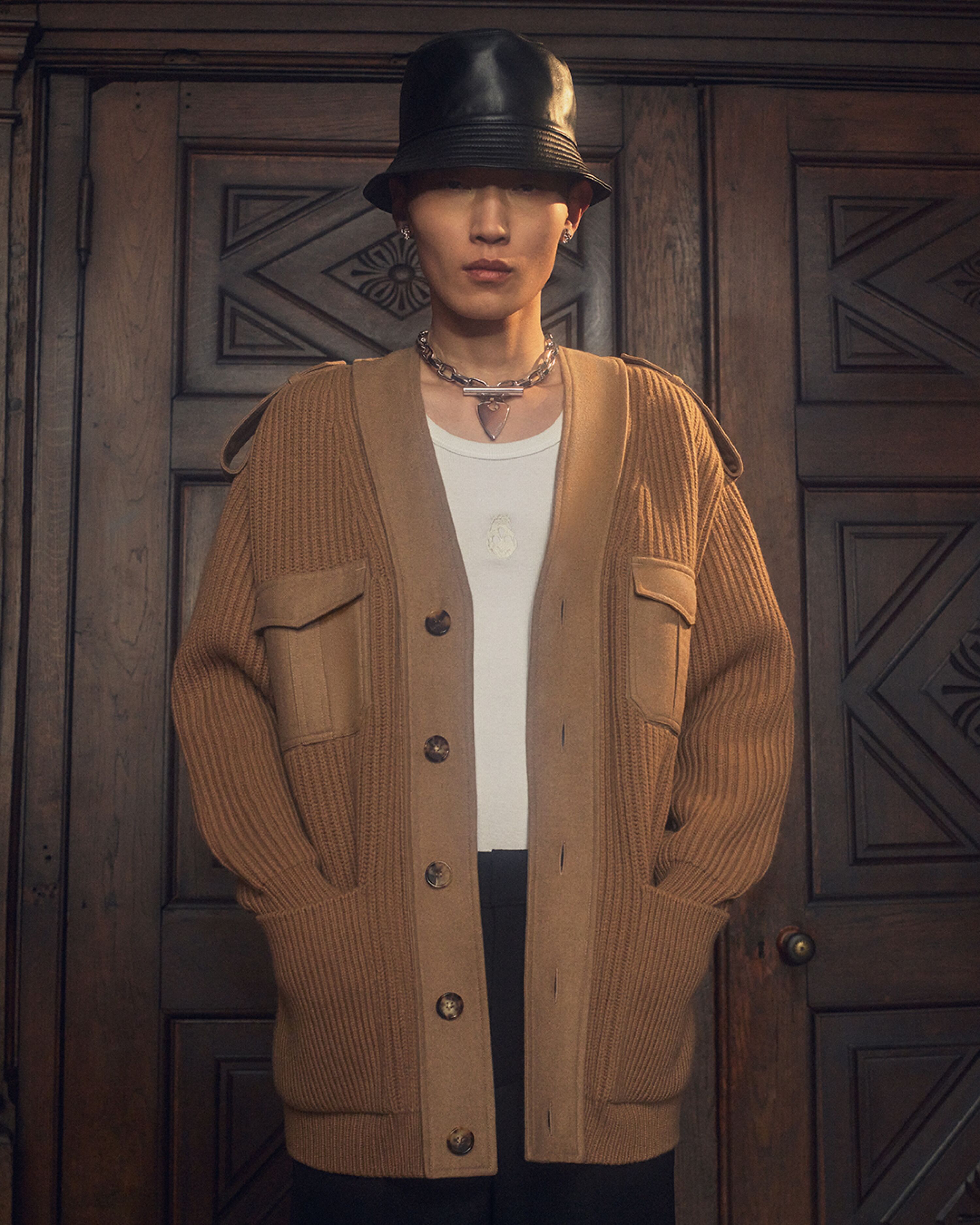 Man in a McQueen tan cardigan and black leather bucket hat