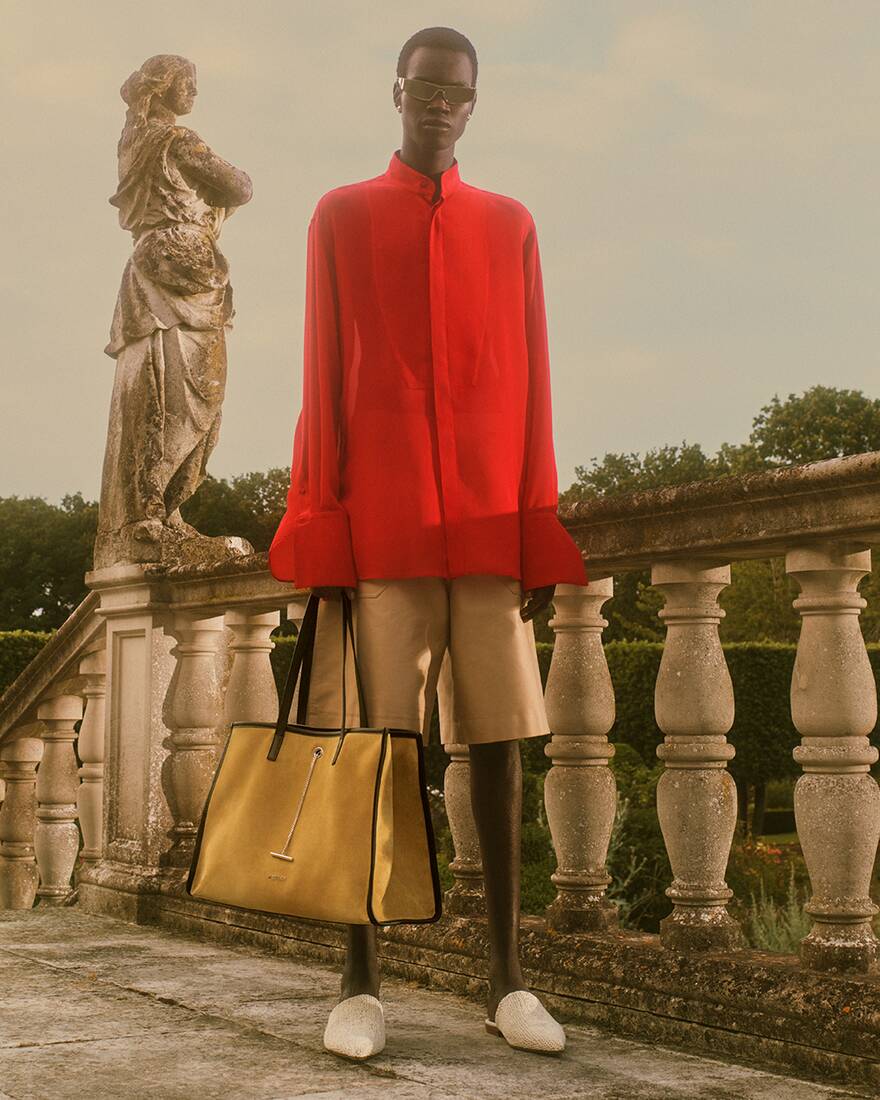 Man in red shirt and brown shorts holding a tote bag