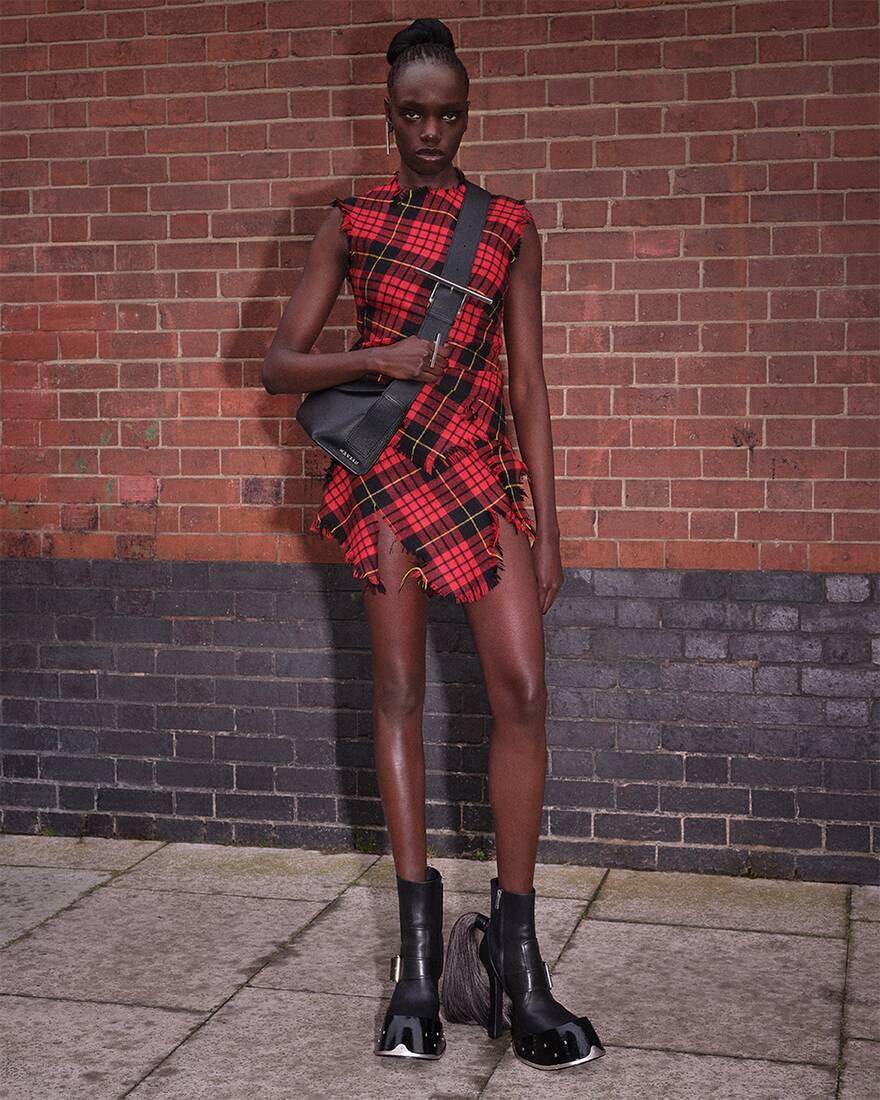 model posing in front of brick wall wearing a tartan dress, crossbody bag, and heeled boots